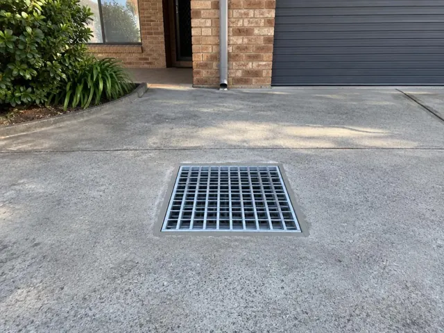Concrete driveway with a square metal grate near a brick home in Warners Bay