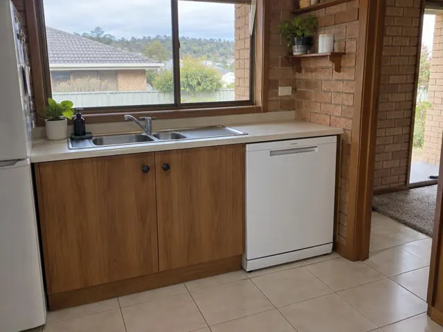 White dishwasher under a kitchen bench beside a sink and tiled floor in Mount Hutton