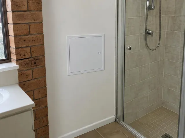 Bathroom wall with a small access panel beside a tiled shower and brick window wall in Cardiff South